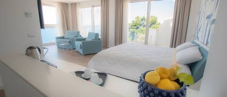 Una habitación de hotel moderna con una cama grande, una zona de estar con dos sillones, una cafetera y un frutero en el alféizar de la ventana.