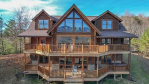 A multi-story log cabin with a balcony, large windows, and a staircase leading to the entrance. - Priceless Views, Game Room, Hot Tub, Firepit & Newly Remodeled! Free Tickets! (Gatlinburg)