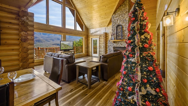 A log cabin interior with a dining area, seating, and a decorated Christmas tree. - Priceless Views, Game Room, Hot Tub, Firepit & Newly Remodeled! Free Tickets! (Gatlinburg)