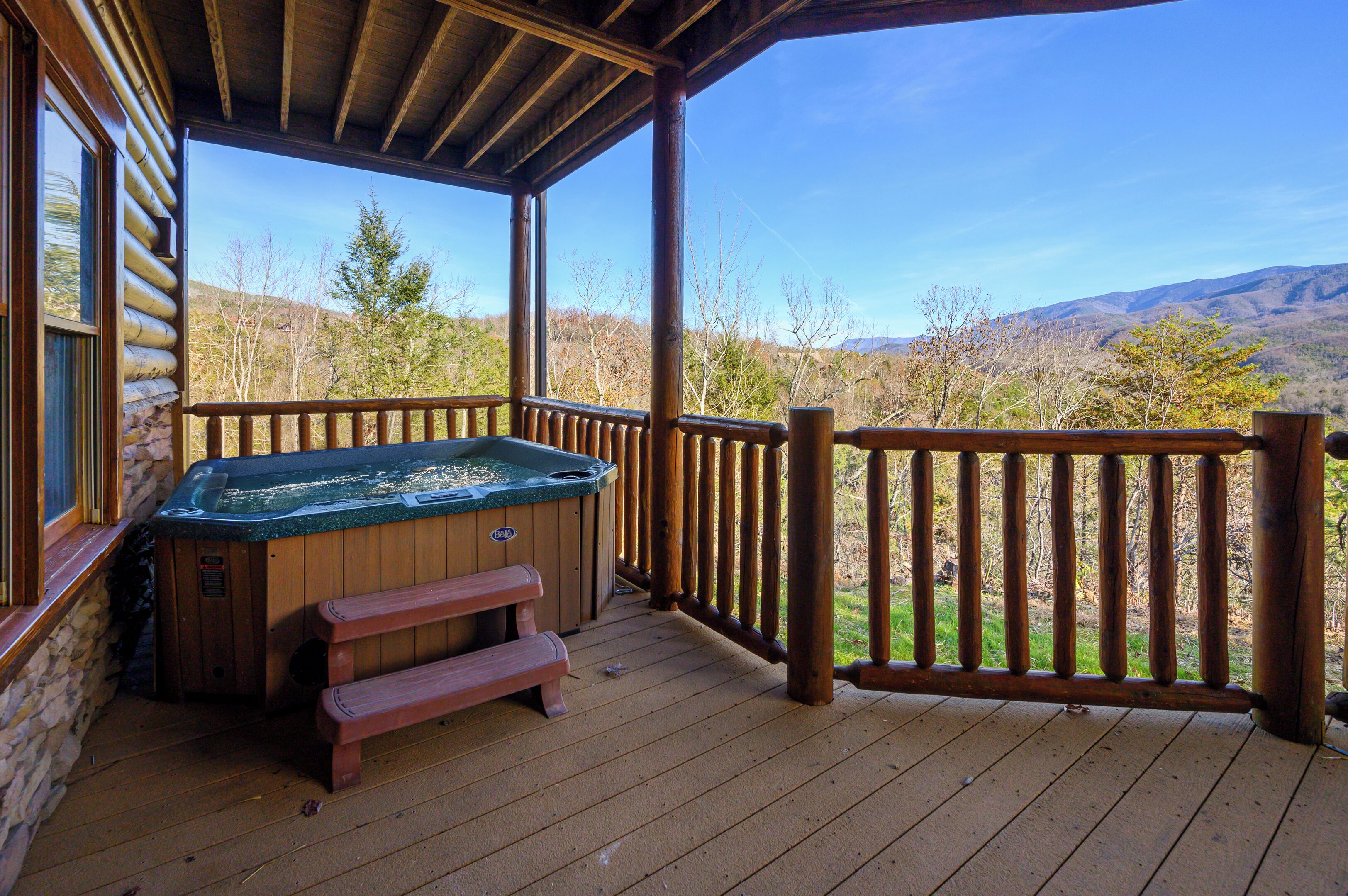 A wooden deck with a hot tub and a wooden bench, overlooking a mountainous landscape.