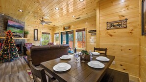 A wooden cabin interior with a dining table set for four, a Christmas tree, and a fireplace.