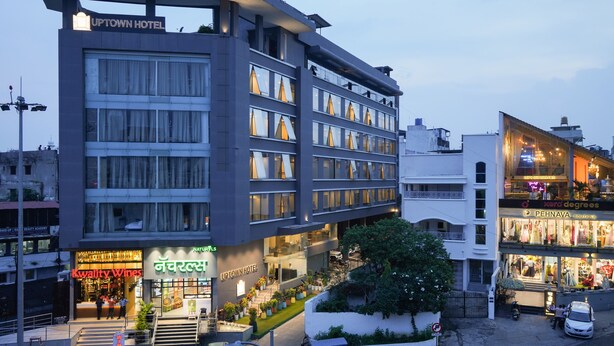 Um hotel de vários andares com design moderno, apresentando uma placa de destaque para 'UPTOWN HOTEL' e uma entrada visível com escadas que levam ao saguão.