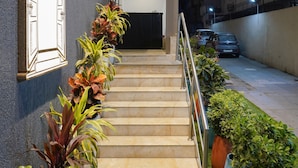 Entrada de hotel com escadas, plantas em vasos e uma placa.