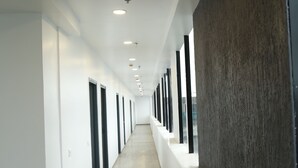 Um corredor comprido e estreito, com paredes brancas, soalho de madeira e uma fileira de janelas de um lado.