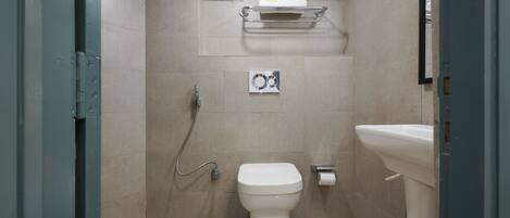 Un baño pequeño con azulejos, un inodoro, un lavamanos, un perchero para toallas y un cabezal de ducha.