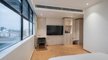 A modern hotel room with a large window, a flat-screen TV, a bed, and a wardrobe.
