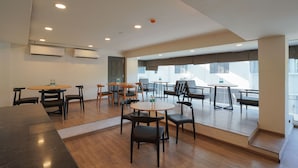Uma sala de jantar moderna com várias mesas e cadeiras, grandes janelas e iluminação no teto.