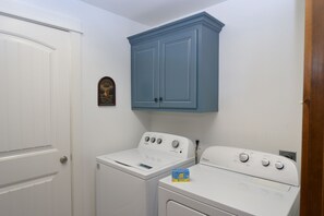 A laundry room with a white washer and dryer, a blue cabinet above the dryer, and a door with a small decorative item. - Fabulous 4BDR that sleeps 12 Cottage with Game Room in Stormy Point Village. (Branson)