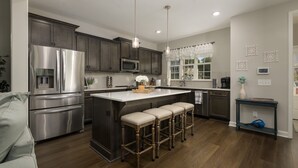 A modern kitchen with stainless steel appliances, a central island with bar stools, and a dining area with a blue console table. - Lake House with Golf Cart (Tullahoma)