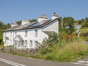 A white house with multiple chimneys, a stone wall, and a road in front. - 1 Sunny Point Cottages (Kendal)