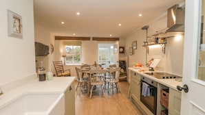 A kitchen with wooden flooring, a dining area with chairs, a window, and a built-in oven. - 1 Sunny Point Cottages (Kendal)