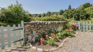A stone wall with a wooden gate, surrounded by a garden with various flowers and plants. - 1 Sunny Point Cottages (Kendal)