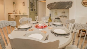 A dining area with a round table set for four, white chairs, and a kitchen in the background. - 1 Sunny Point Cottages (Kendal)
