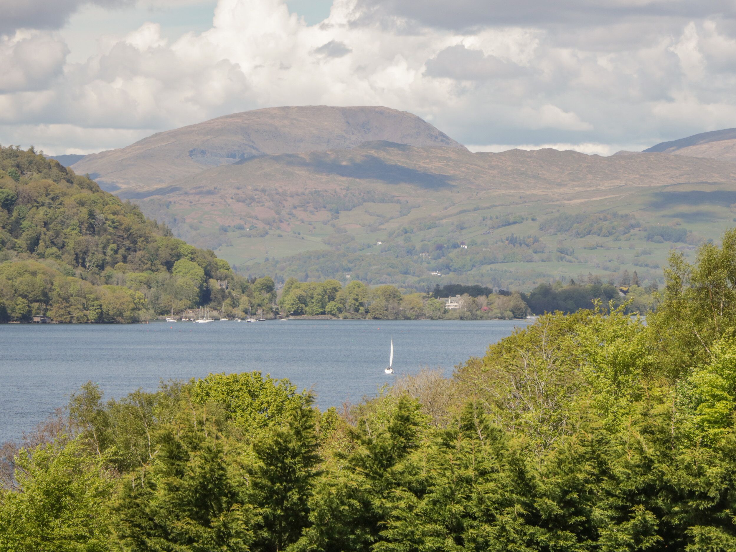 A lake surrounded by hills with a sailboat and a small building on the shore.