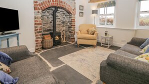 A cozy living room with a stone fireplace, comfortable seating, and a television. - 1 Sunny Point Cottages (Kendal)