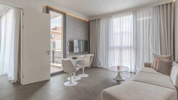 Una habitación de hotel moderna con zona de comedor, sofá y televisor.