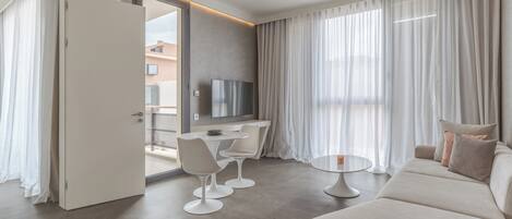 A modern hotel room with a dining area, a sofa, and a TV.