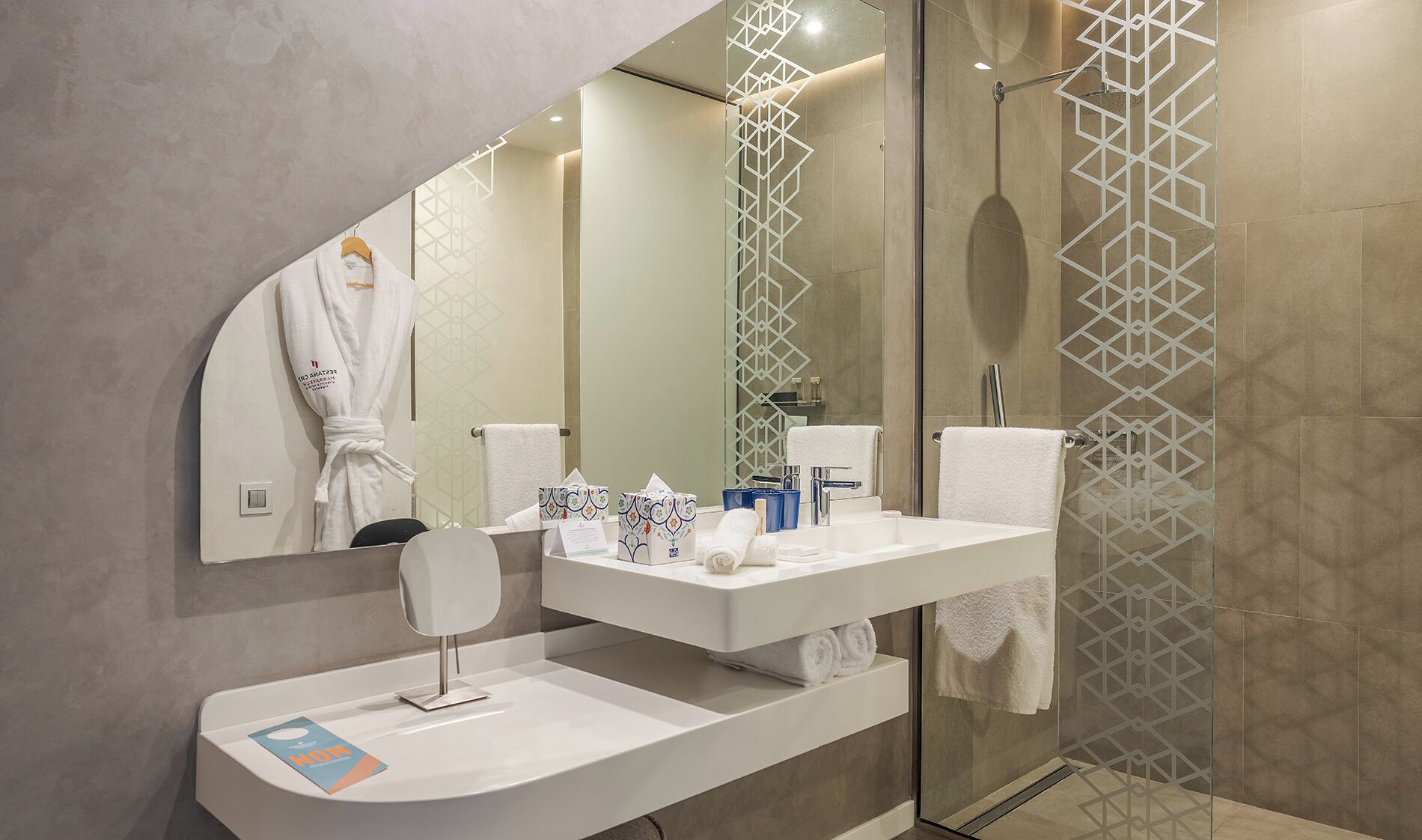 A modern bathroom with a large mirror, a white vanity, a shower with a glass door, and a towel rack.