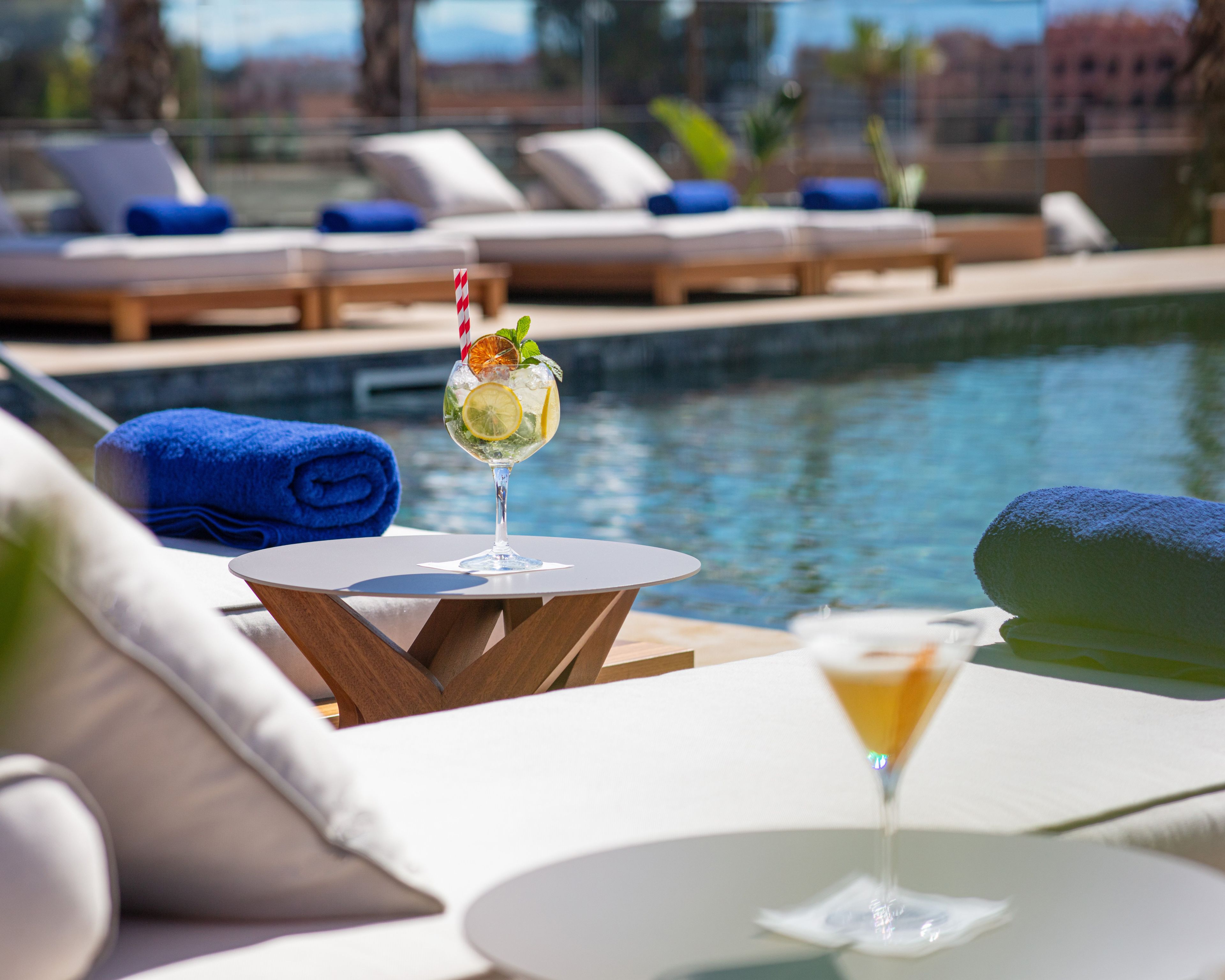 A poolside area with lounge chairs, a table with a drink, and a view of the pool.