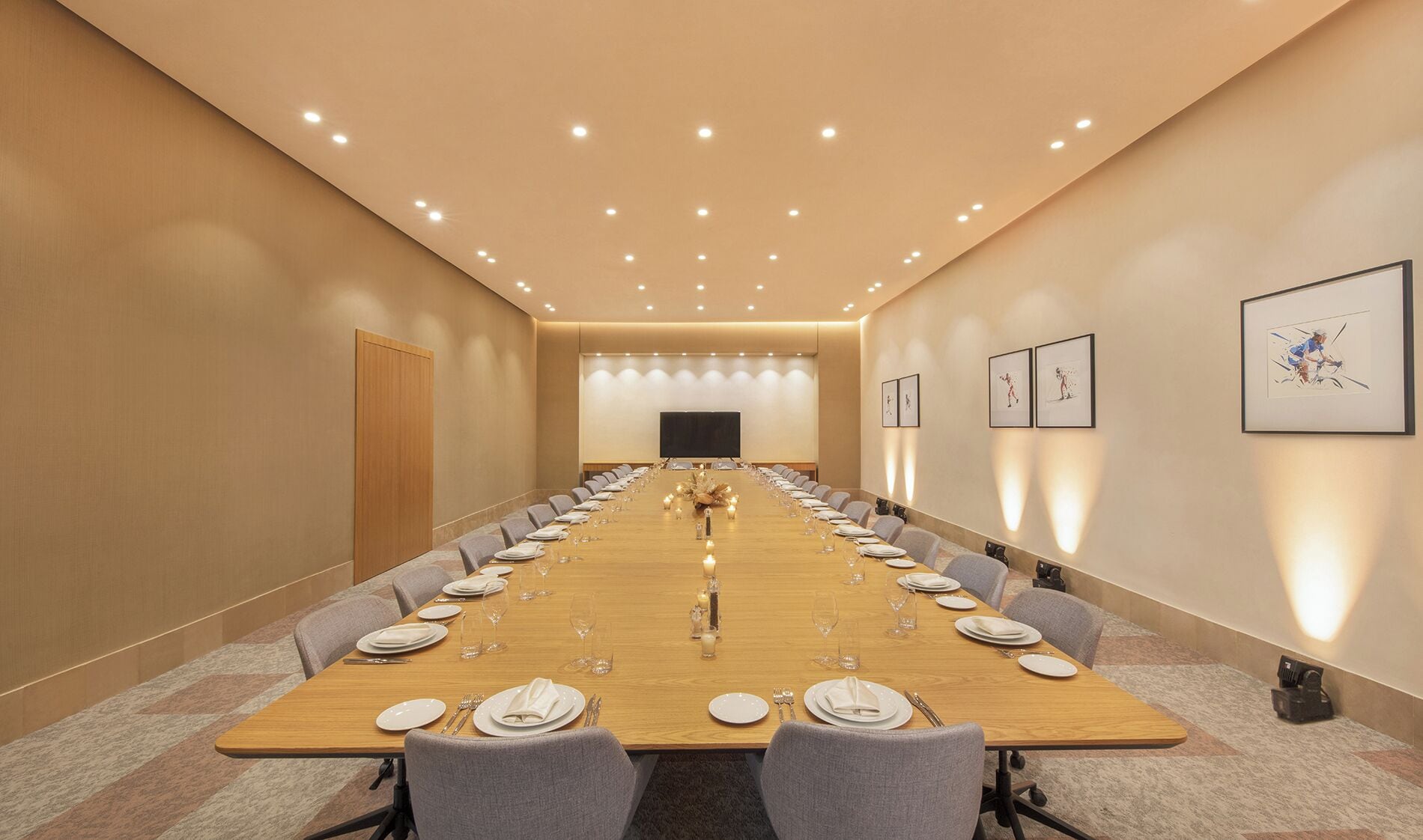 A conference room with a long table set for a meeting, equipped with a projector screen and framed artwork on the walls.