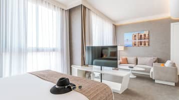 A modern hotel room with a large bed, a TV, a sofa, and a dining table.