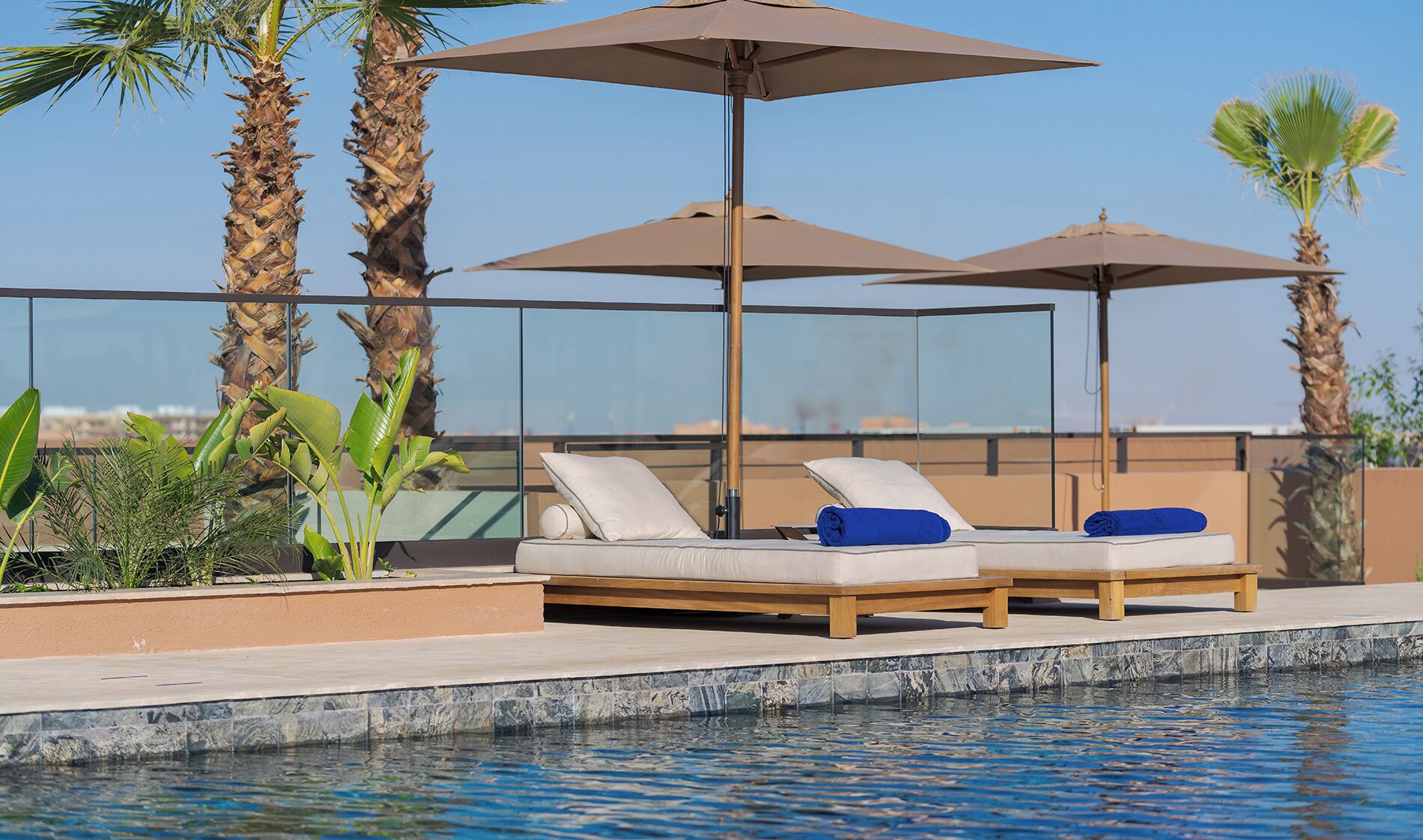 A poolside area with two sun loungers, a glass balustrade, and palm trees.