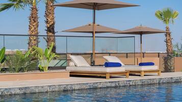 A poolside area with two sun loungers, a glass balustrade, and palm trees.