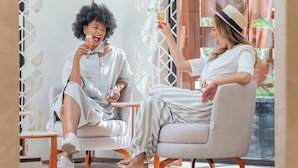 Dos personas sentadas en sillas modernas en una habitación con paredes de diseño geométrico y un ventanal grande.