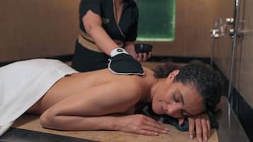 A person receiving a back massage in a room with a wooden floor and a green towel hanging on the wall.