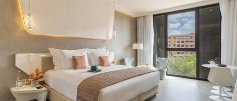 A modern hotel room with a large bed, bedside tables, a desk, and a balcony with a view of buildings.