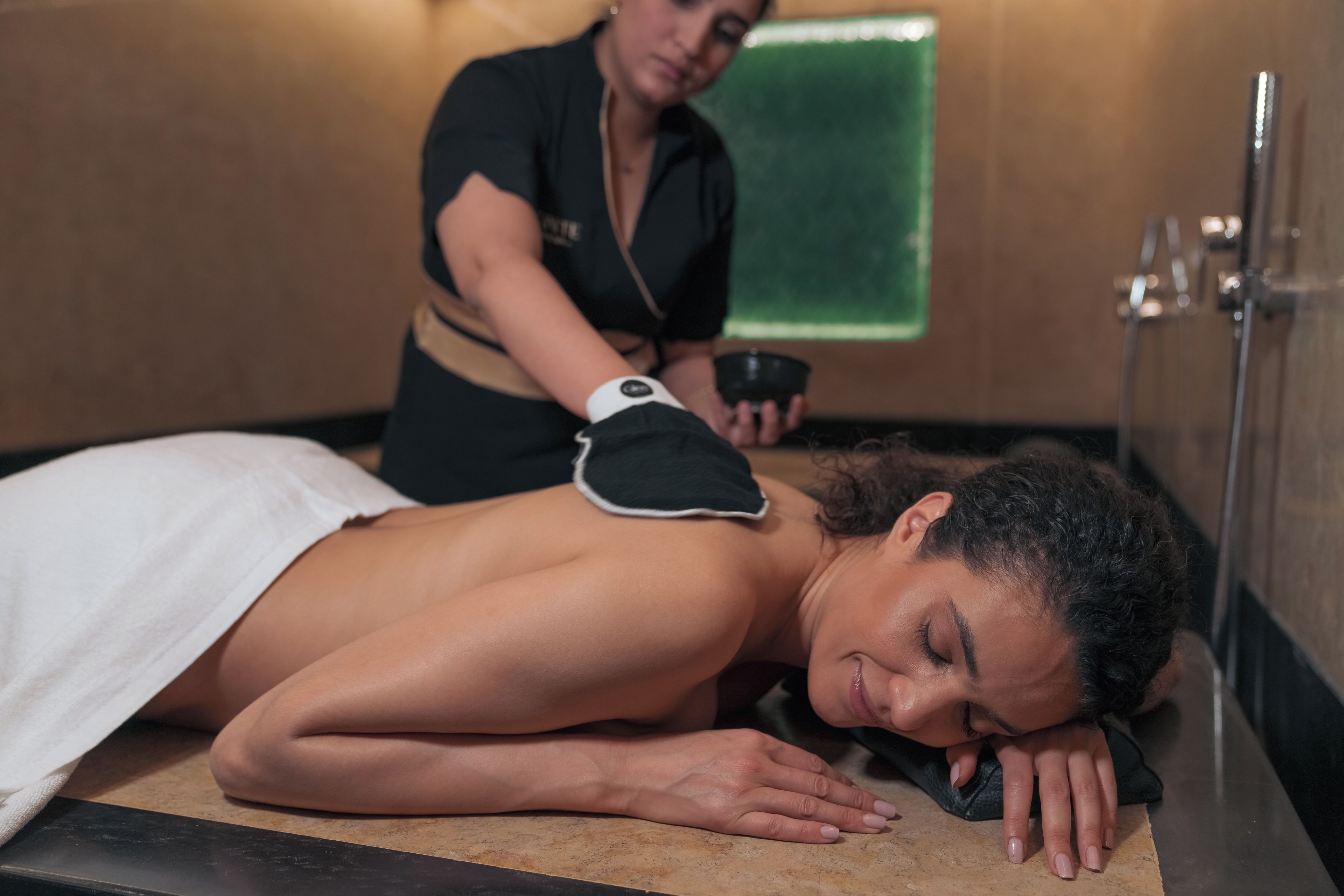 A person receiving a massage in a room with a massage table, a green towel, and a massage therapist.