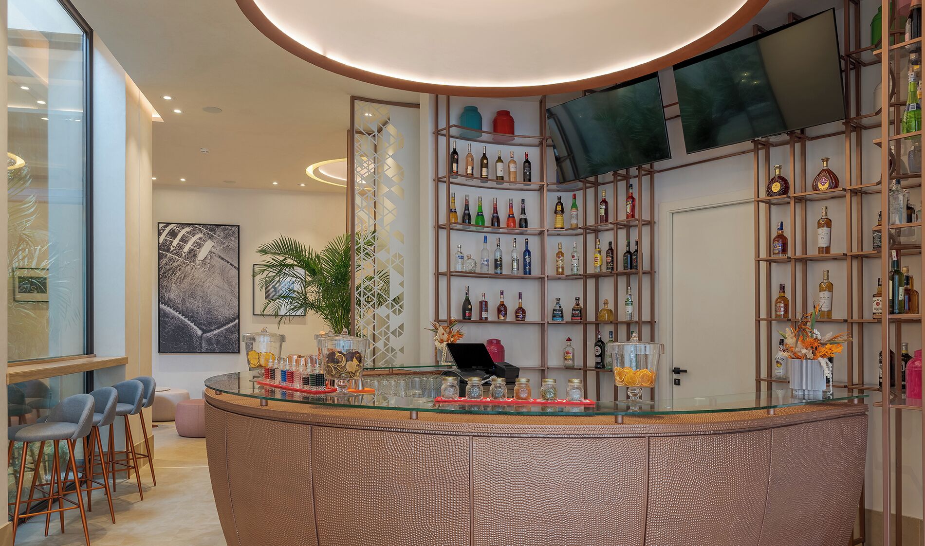 A modern bar area with a glass counter, a laptop, and a variety of bottles.