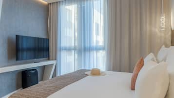 A hotel room with a large bed, a flat-screen TV mounted on the wall, and a window with sheer curtains.