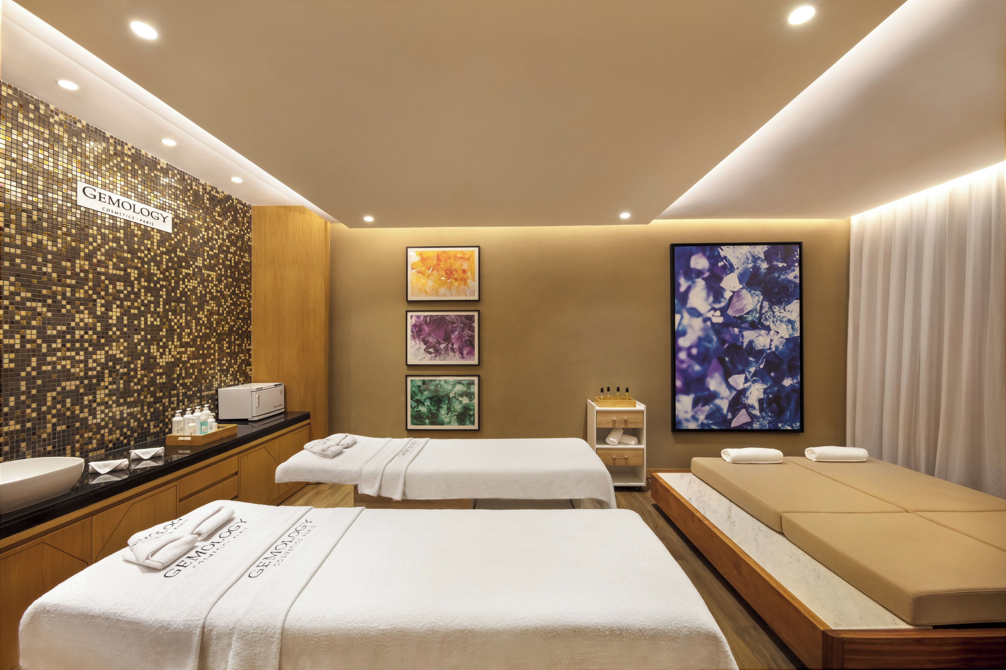Un spa moderno con dos camillas de masaje, un mueble de madera con artículos de aseo y un televisor montado en la pared.