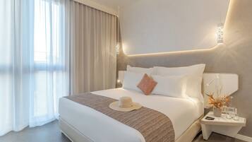 Een moderne hotelkamer met een groot bed, een nachtkastje met een lamp en uitzicht op het omliggende landschap door dunne gordijnen.