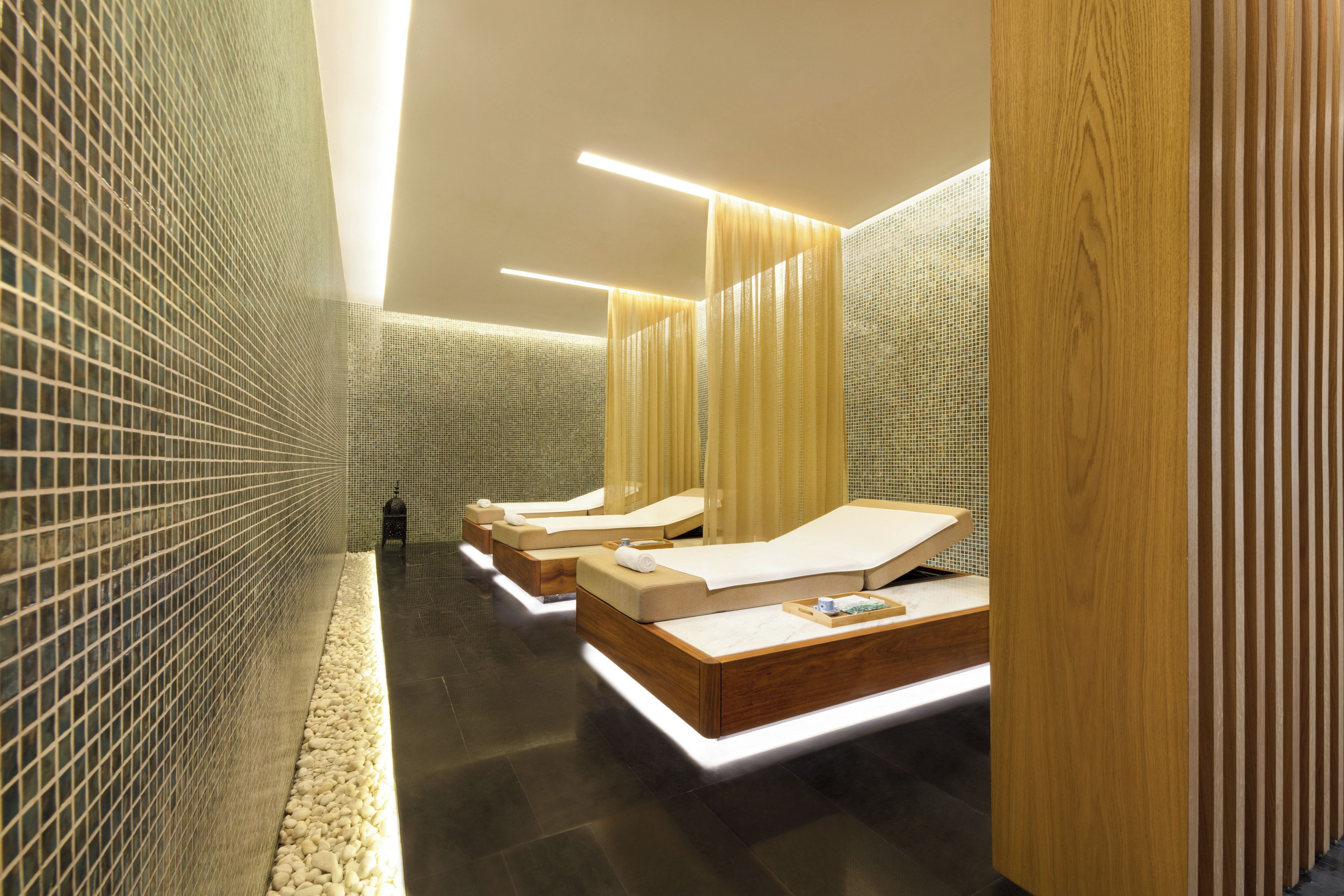 A modern spa room with three massage beds, a tiled floor, and a wooden partition.