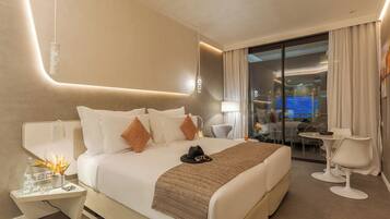 A modern hotel room with a large bed, a sitting area with a table and chairs, and a view of a cityscape through the glass door.