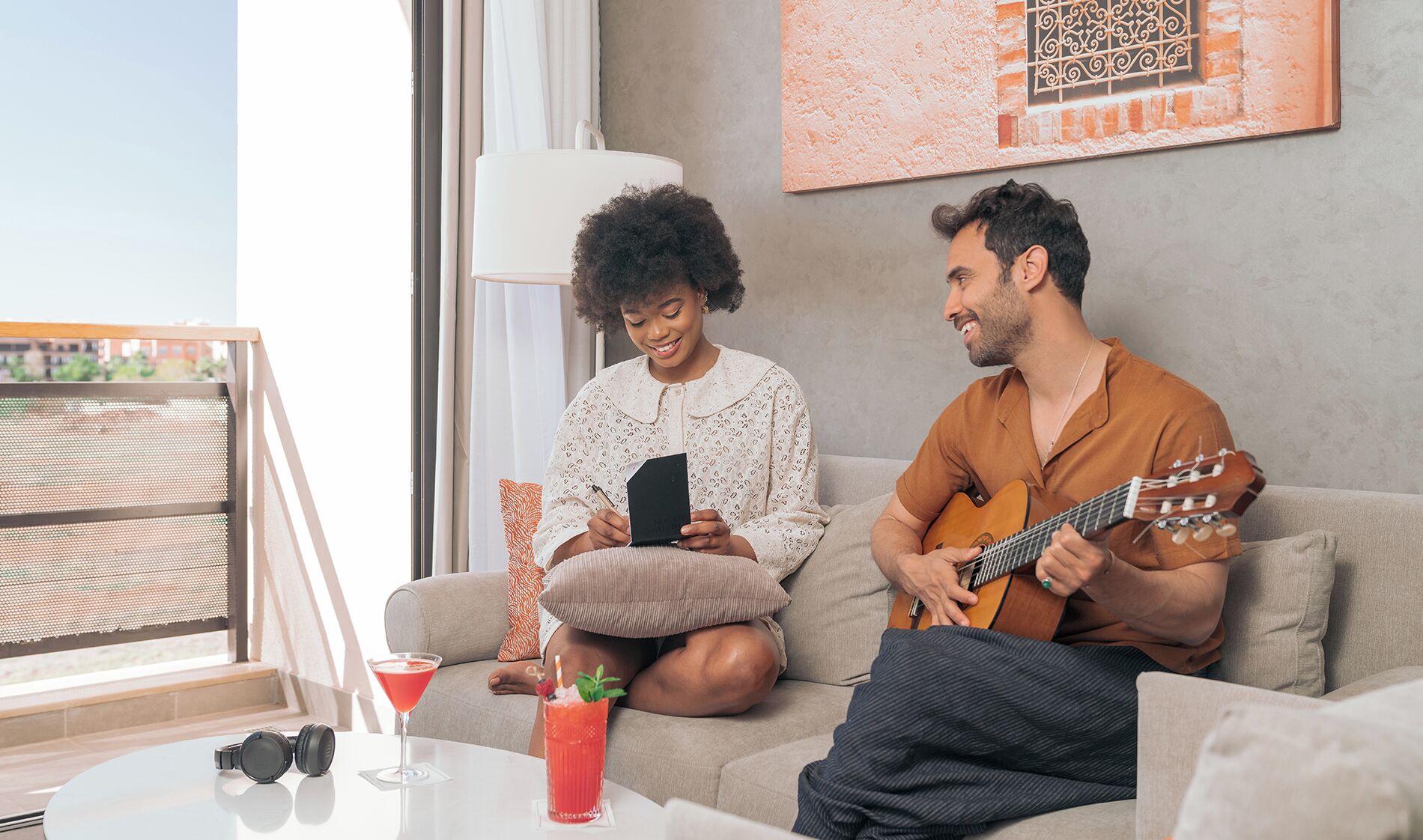 Un salon moderne avec un canapé, une table basse sur laquelle sont posées des boissons, et une vue sur le balcon.