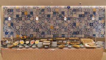 A buffet with various food items and a patterned tile wall in the background.