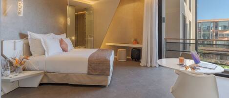 A modern hotel room with a bed, bedside table, lamp, and a balcony with a laptop and a suitcase.