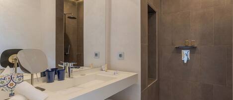 A modern bathroom with a large mirror, a shower, and a vanity with a towel and toiletries.