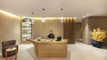 A reception desk with a woman seated behind it, a wooden counter, and a display of products in the background.