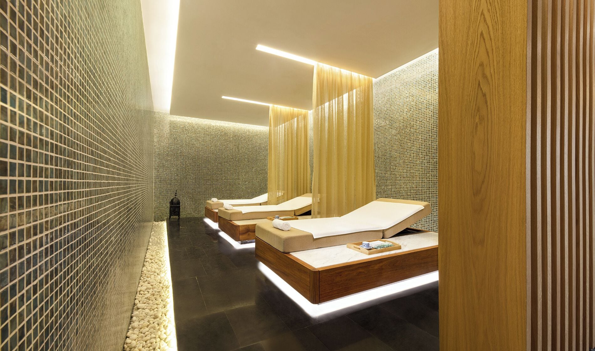 Ein moderner Wellnessraum mit drei Holzbettliegen, einer gefliesten Wand und einem Holzboden.