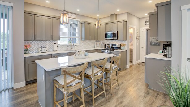 A modern kitchen with a central island, wooden chairs, and a microwave.
