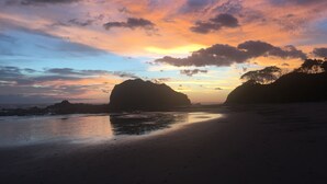 Een strand met een zonsondergang, kalm water en verafgelegen rotsformaties.