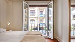 A bedroom with a bed, a nightstand, and a view of a balcony with a railing. - Always Easy I Larroca (San Sebastián/Donostia)