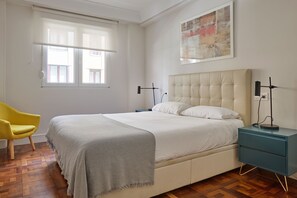 A bedroom with a bed, a chair, a nightstand, a lamp, and a painting on the wall. - Always Easy I Larroca (San Sebastián/Donostia)