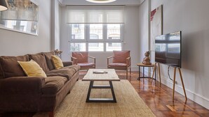 A living room with a brown sofa, two chairs, a coffee table, a TV on a stand, and large windows. - Always Easy I Larroca (San Sebastián/Donostia)