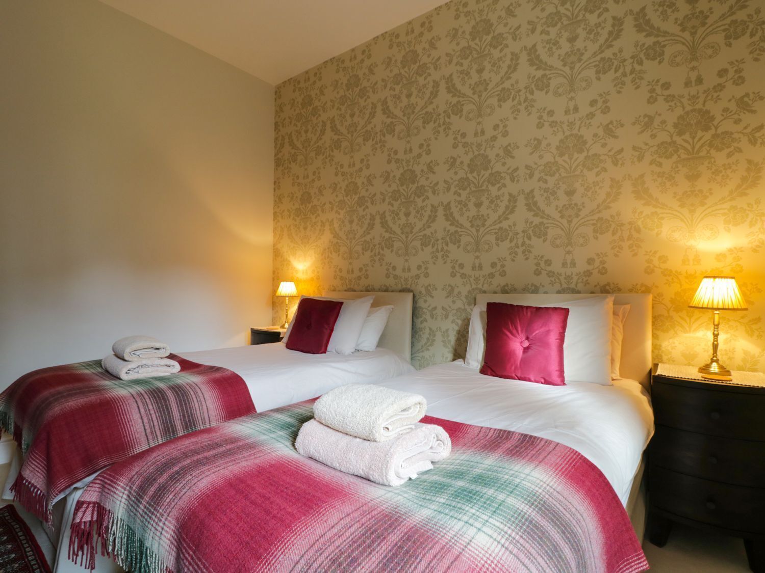 Une chambre d’hôtel avec deux lits, chacun recouvert d’une couverture rouge et blanche, avec des oreillers blancs et un coussin décoratif rouge. Deux lampes de chevet sont posées sur des tables de nuit en bois.