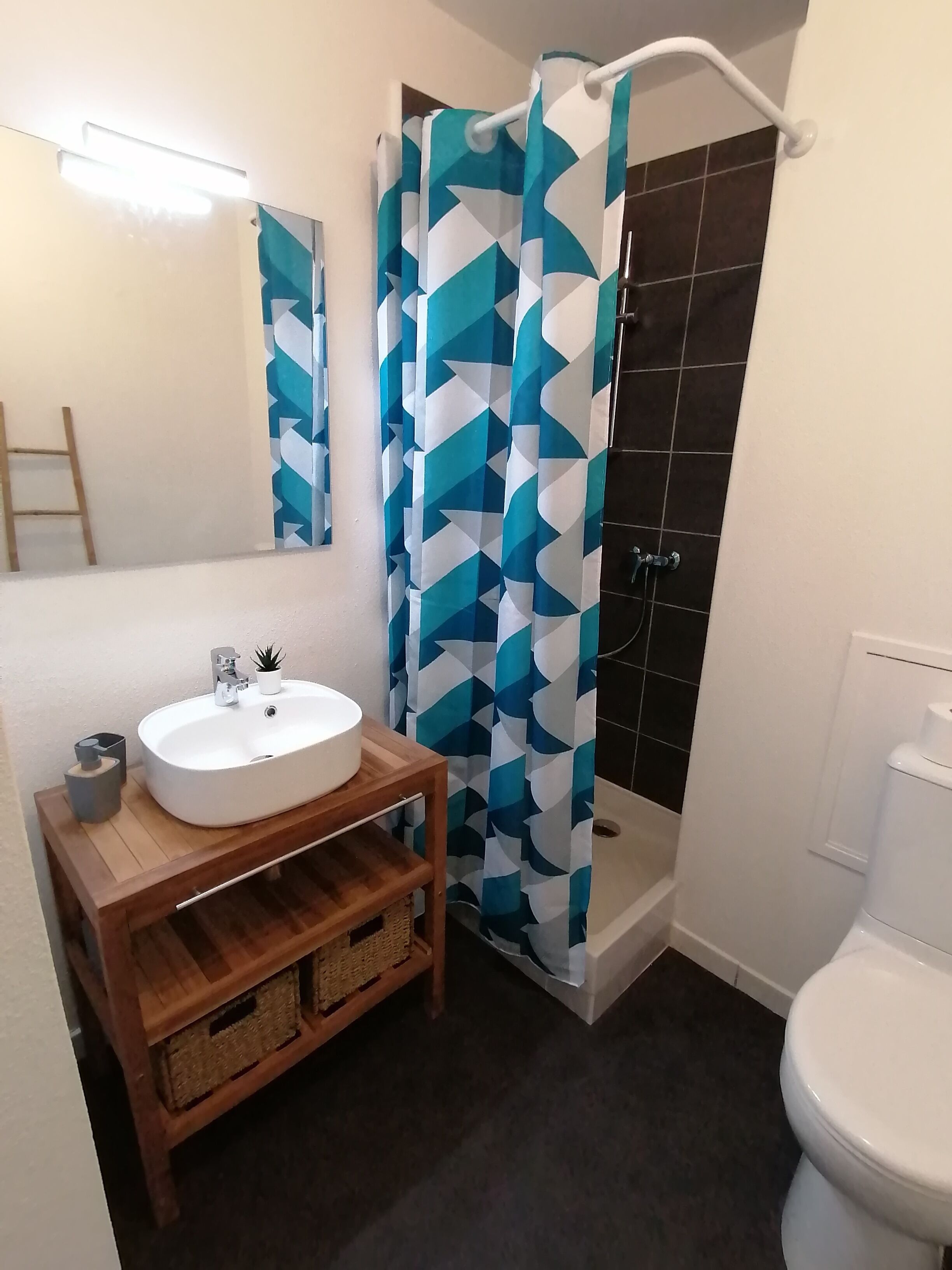A bathroom with a white sink, wooden vanity, a shower with a geometric patterned curtain, a toilet, and a mirror.